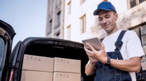 Courier using digital tablet to manage parcel deliveries from van