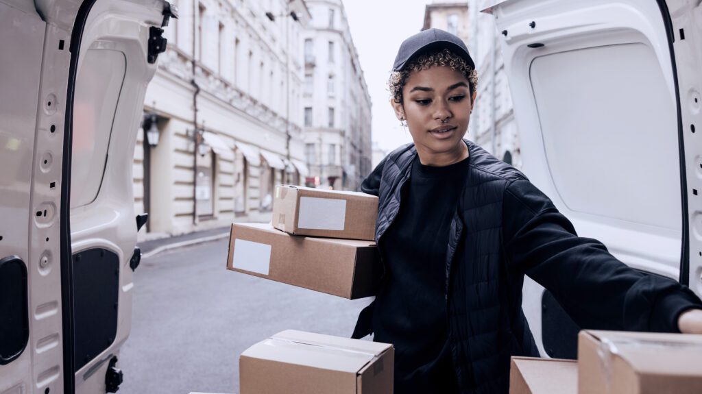Female courier unloading multiple parcels from van for city delivery route